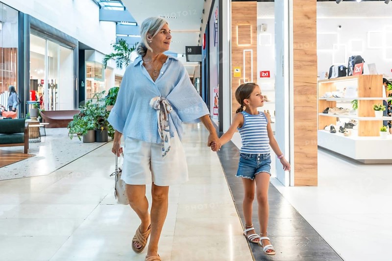 Grandmother and granddaughter enjoying their time together, walking hand in hand through a modern shopping mall, exploring stores and spending quality leisure time