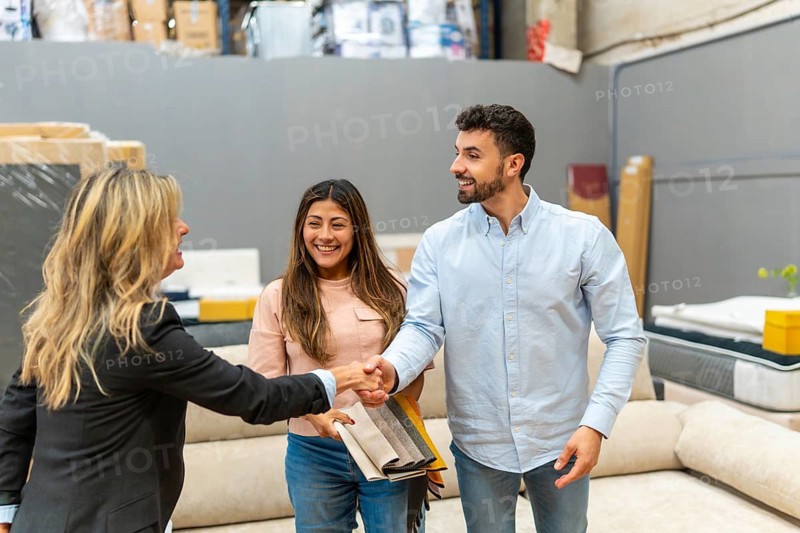 Salesperson shaking hands with a young male customer, while his female partner holds fabric swatches, symbolizing successful deal and good customer service in a home improvement store