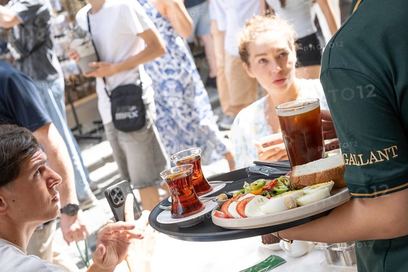 Istanbul, Turkey. August 7th 2026. A restaurant waiter serves tourists a traditional Turkish breakfast including glasses or tea at a pavement Cafe near the Galata Tower, Istanbul, Turkey
