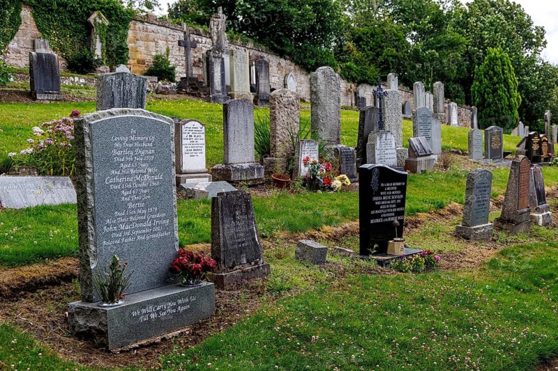 Rows of weathered headstones fill the cemetery beside Rosslyn Chapel in Roslin, Midlothian, Scotland, United Kingdom