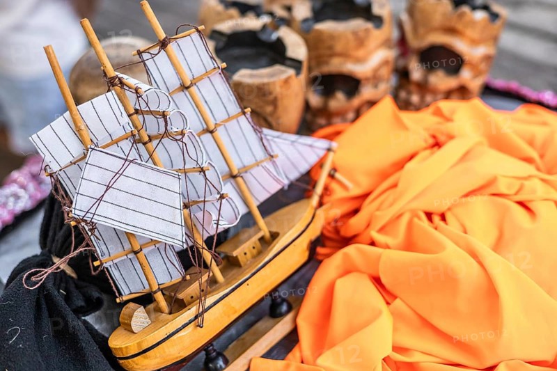 A detailed model ship with white sails rests on a colorful fabric background. Decorative skulls are visible, adding a unique touch to the scene