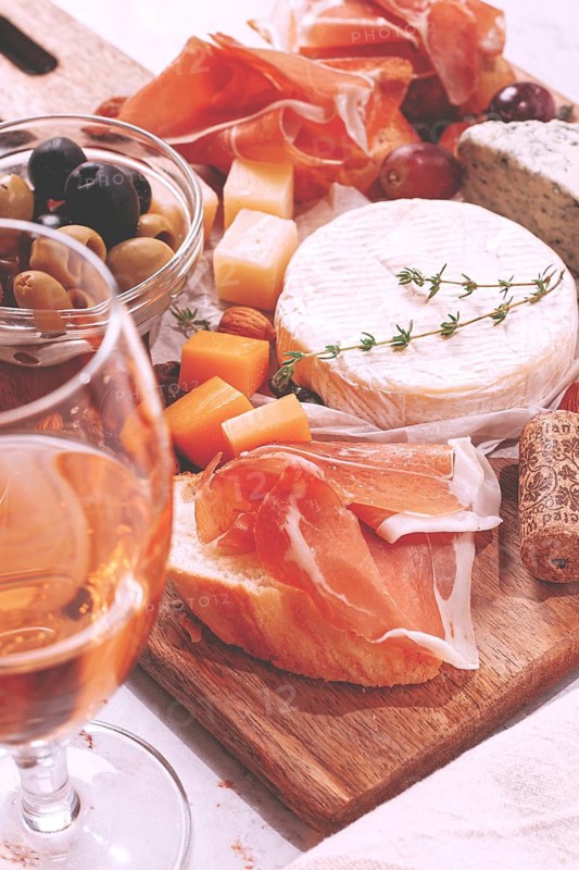 People enjoy a cheese and charcuterie board with various cheeses, meats, fruits, nuts, and olives alongside glasses of white wine. This scene shows a social gathering in a home setting. no people