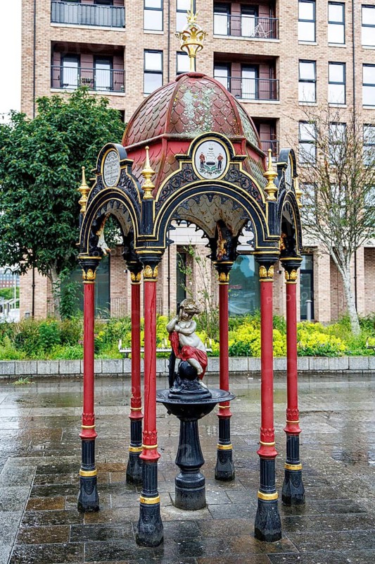 Ornate red and gold cast iron Victorian drinking fountain dedicated to Dr John Aitken, standing at Govan Cross, Glasgow, Scotland, United Kingdom