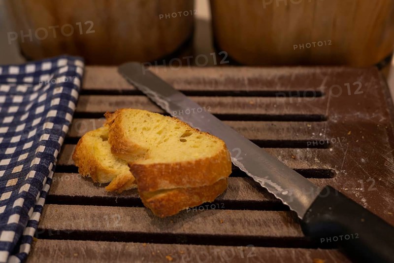 Sliced bread rests on a wooden cutting board next to a knife, with baskets of whole loaves in the background. Homemade freshly baked bread