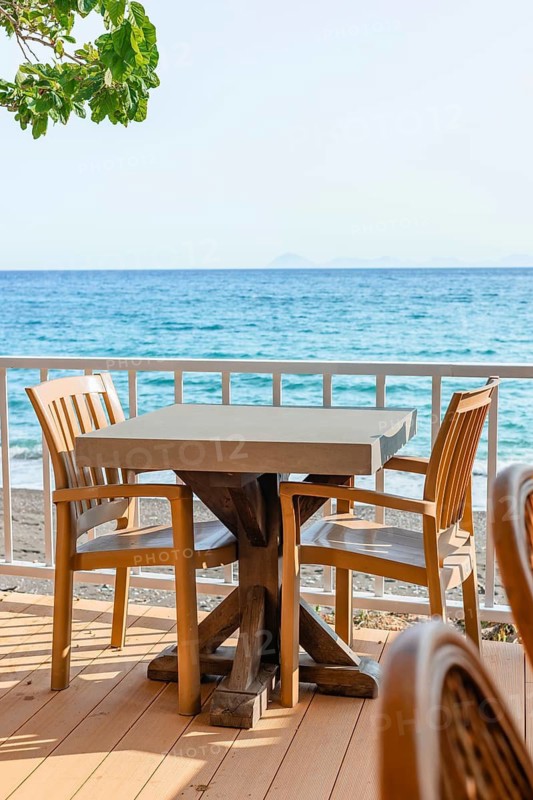 Brightly lit seaside dining space features wooden tables and chairs with stunning ocean views, perfect for relaxation