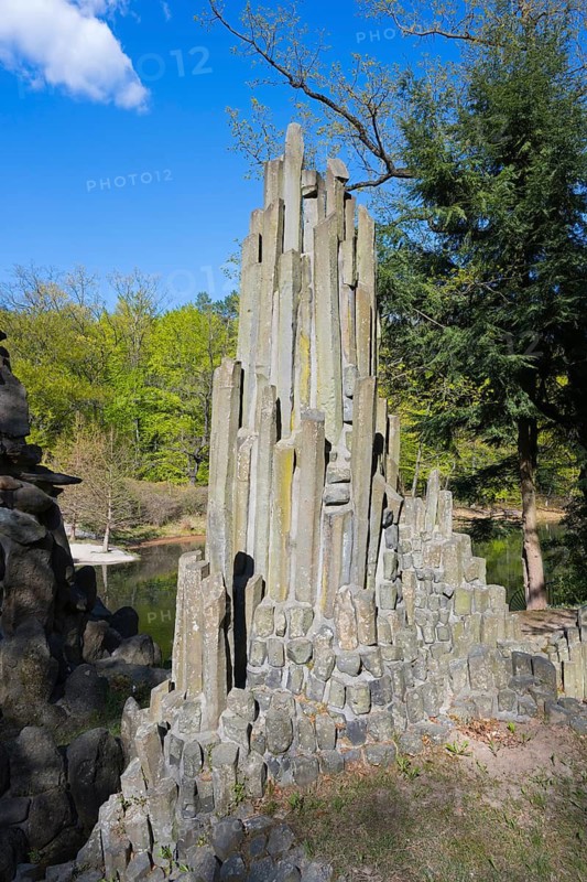 Massive, vertical stone column rises against a wooded background in the sun, at the Rakotz Bridge, Devil's Bridge, Rakotzsee, arched bridge, reflection, basalt organ, Kromlau, Görlitz district, Saxony, Germany