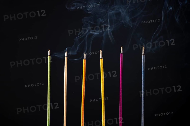 Six coloured incense sticks emit smoke, dark background