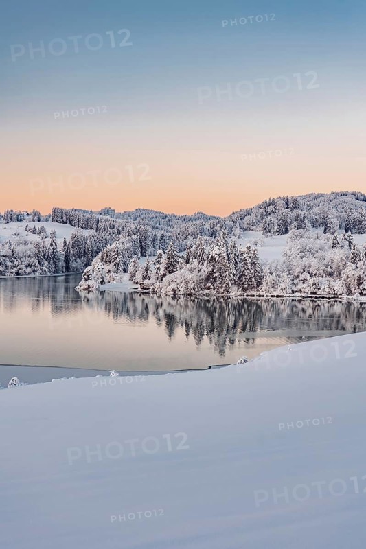 Dawn and sunrise at the wintry Forggensee in a snow-covered winter landscape in the foothills of the Alps in the Allgäu in Bavaria, Germany