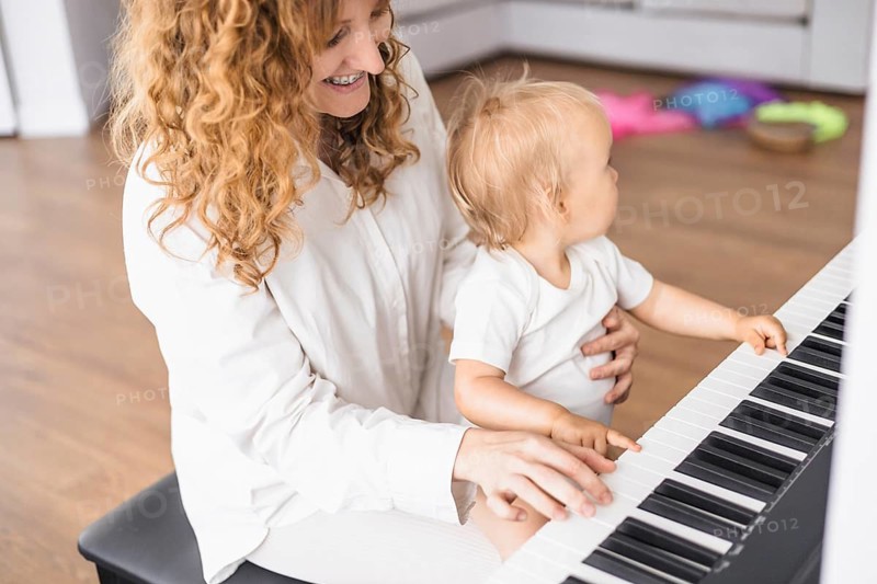 Mother smiling as she holds her child on her lap while playing the piano