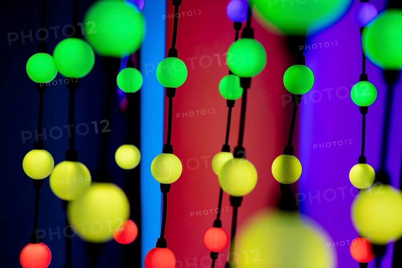 Colorful decorative lights in various shades of green, yellow, and red hanging against a vibrant background. The scene creates a festive atmosphere
