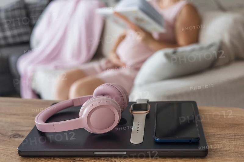 Digital detox during a cozy afternoon at home with headphones and a book in hand. Pregnant woman relaxing on coach