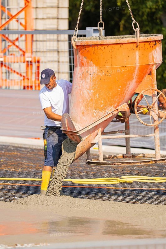 A construction worker pours concrete from a large orange hopper onto a surface, Parkhausbau, Calw, Germany