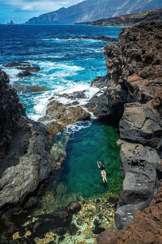 Woman enjoying swimming in a natural clear water pool formed by volcanic rocks and ocean waves during a relaxing vacation on the coast of el hierro island in the canary islands, spain