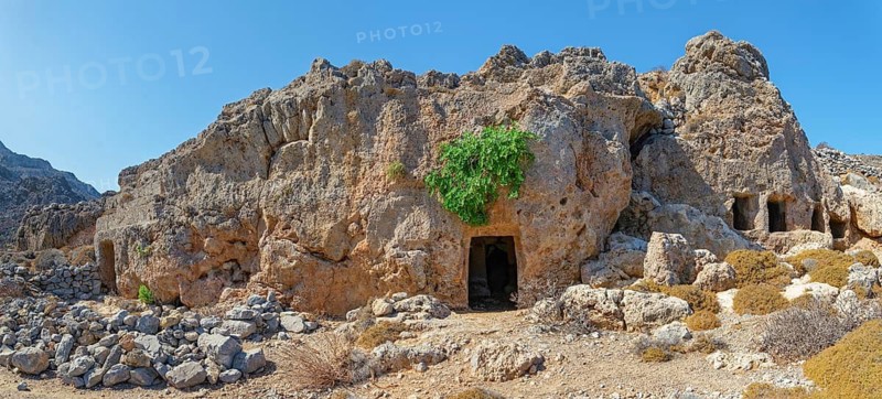 Historic cave entrances of the ancient Dorian city of Vrougounda in a rock formation with green plants, Dorian city of Vrougounda, Avlona, Karpathos, Greece