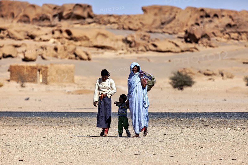 Family in traditional dress walking through a desert landscape with rocks in the background, woman in the Sahara in Algeria