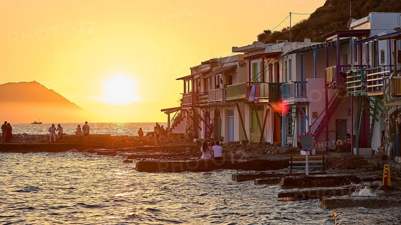 Colourful buildings along the coast at sunset with silhouettes of people and warm light, boathouses, boat garages, Syrmata, fishing village, coastal town, climate, Milos, Cyclades, Greek islands, Greece