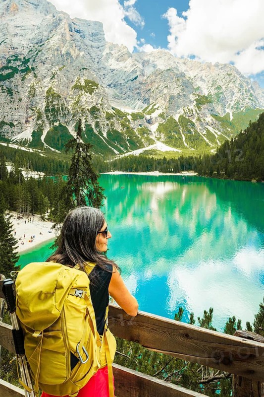 Woman Hiker traveler or visitor with Yellow Backpack Looking at Lago di Braies Dolomites Italy. Famous hiking destination Europe