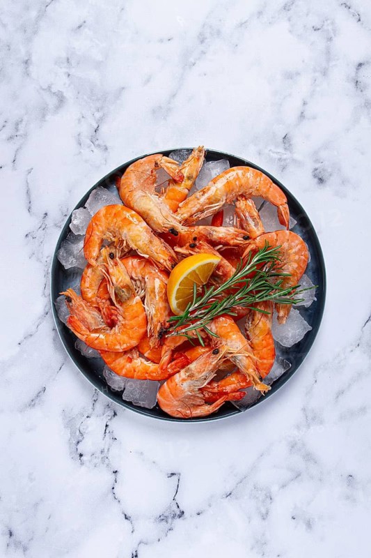 Freshly frozen shrimp on ice, with lemon and rosemary, on the marble table, top view, no people