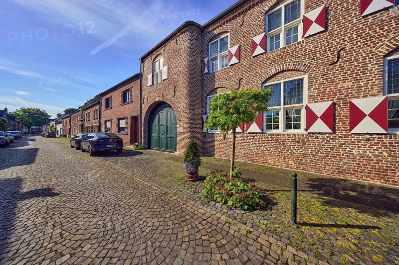 House Wachtendonk, old town center, historic brick building, façade with windows, shutters and wall anchors, gate, entrance gate, street, barrier bollard, sidewalk, street, paving stones, parking strips with cars, flower pots, trees, blue sky, cirrus clouds, Neustraße, Wachtendonk, Kleve district, North Rhine-Westphalia, Germany