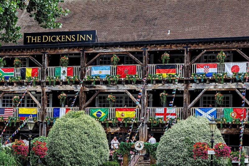 Rows of national flags and hanging flower baskets line the tiered wooden balconies of The Dickens Inn, a converted eighteenth century riverside warehouse near Tower Bridge that took on its current name and pub use in 1976 through a family connection to Charles Dickens, St Katherine's Dock, London, England, United Kingdom