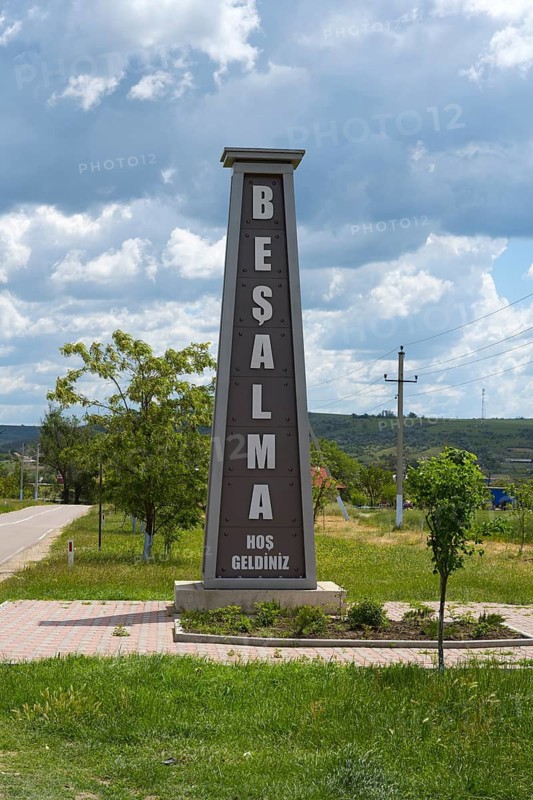 Signpost with writing in front of a green field and cloudy sky, place name with a welcome message in Gauga language, Besalma, Be?alma, Comrat district, Komrat, autonomous region of Gagauzia, Republic of Moldova, Moldova