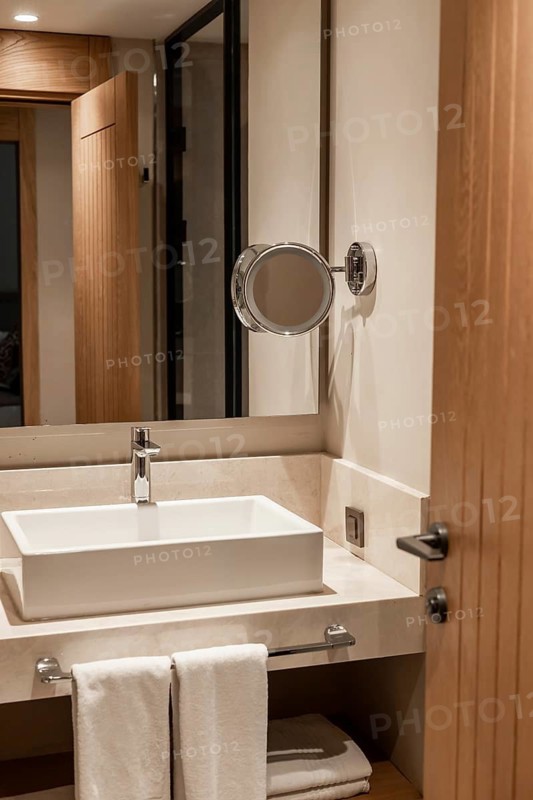 Modern bathroom interior with a white sink, wooden door, and mirror. Clean and minimalist design with neutral colors. luxury hotel
