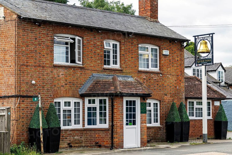 The historic former Bell pub with white porch, sash windows and topiary planters, now trading as Lounge India Restaurant, Bierton, Buckinghamshire, United Kingdom