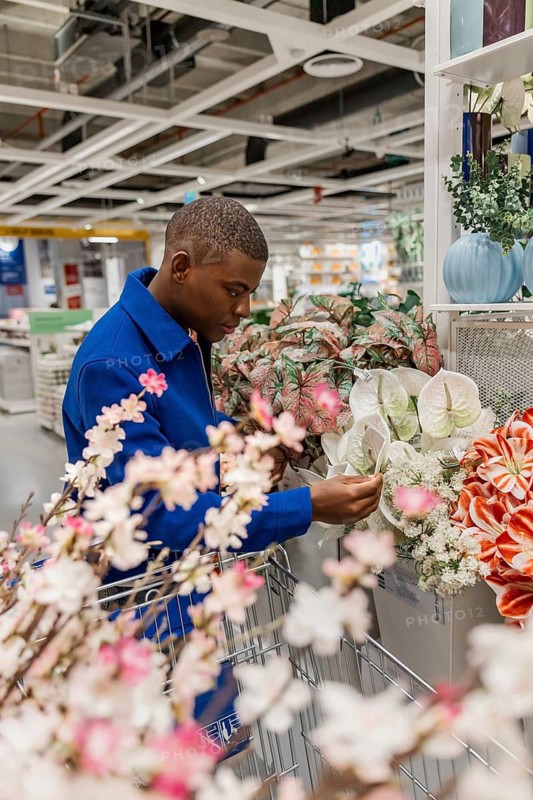 A man is looking at flowers while shopping in a store that specializes in home decor. The scene shows various types of flowers and decorations on display