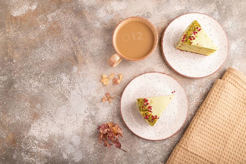 Pistachio green cake with cup of coffee on brown concrete background with beige textile, copy space, top view, flat lay