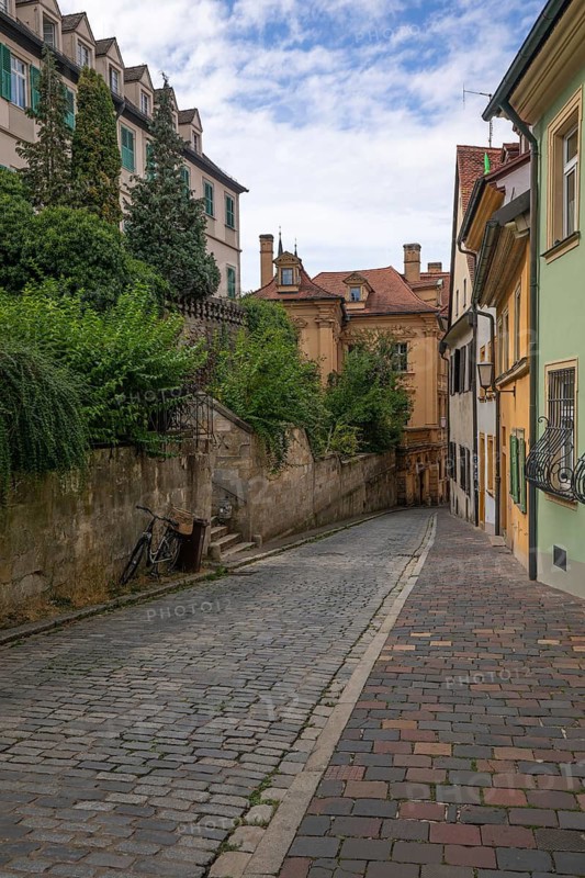 20 August 2026, A bicycle stands on a cobblestone street lined with historic buildings in Bamberg, Bavaria, Germany
