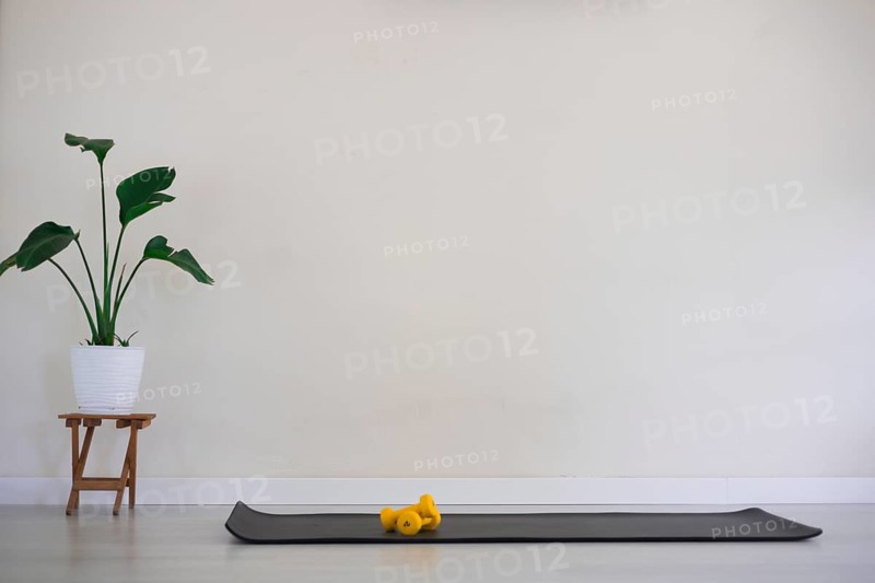 Minimalist room with a black yoga mat and yellow dumbbells beside a plant