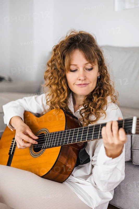 Woman with curly hair playing a guitar in a relaxed setting