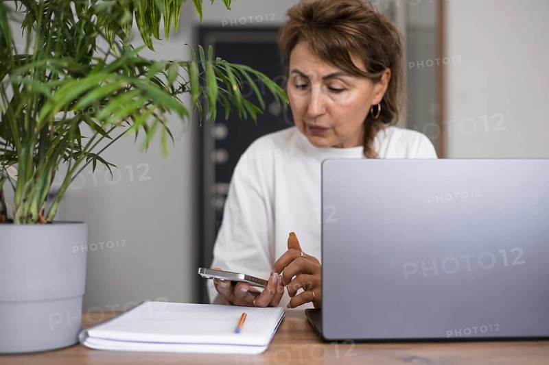 Portrait serious pensive mature business woman in white clothes thinking or making decision, using laptop computer at home, holding pen, brainstorming on creative ideas, problem solving