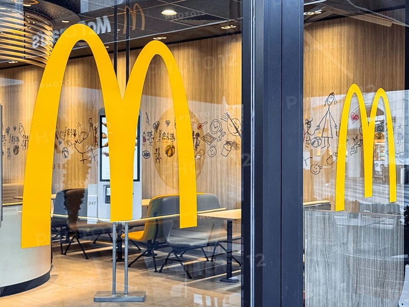 Turkiye, Antalya - 12.03.2025: McDonalds logo. Window door large yellow arches, symbolizing the fast food restaurant. Inside, kiosks await customers while the evening light casts a welcoming glow
