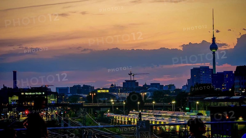 View of railway tracks from Modersohn Bridge, skyline at dusk with television tower and illuminated buildings in the background, Friedrichshain, Berlin