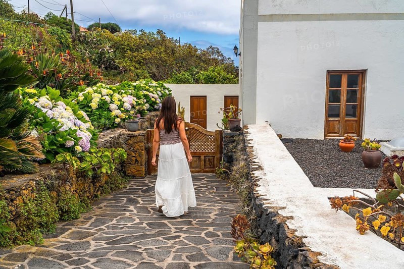 Woman in white dress exploring a beautiful traditional garden with lush hydrangeas and volcanic rock walls, enjoying island travel and nature on el hierro