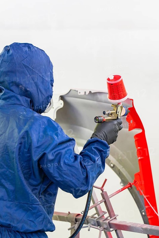 Skilled worker in blue protective clothing paints a car part with red paint, Painter, Calw, Germany