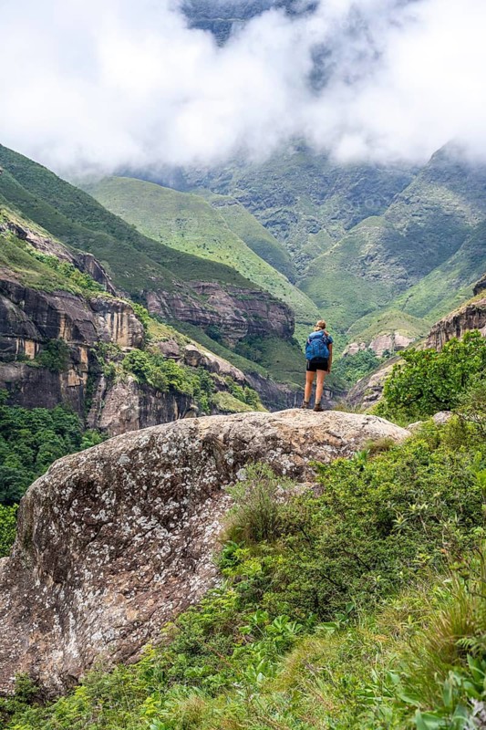 Female hiker standing in front of landscape with mountains and fog, Drakensberg National Park, KwaZulu Natal, South Africa
