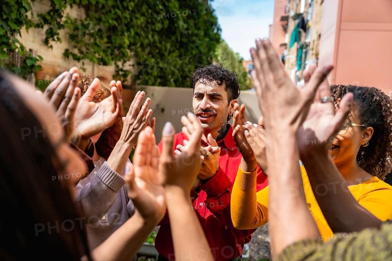 Diverse people clapping hands in a circle enthusiastically supporting and celebrating a man, symbolizing community, mental health progress, and successful group therapy
