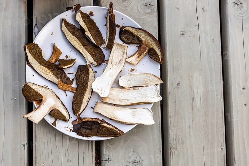 Dried mushrooms arranged on a white plate. The mushrooms are various shades of brown and white, placed on a wooden surface