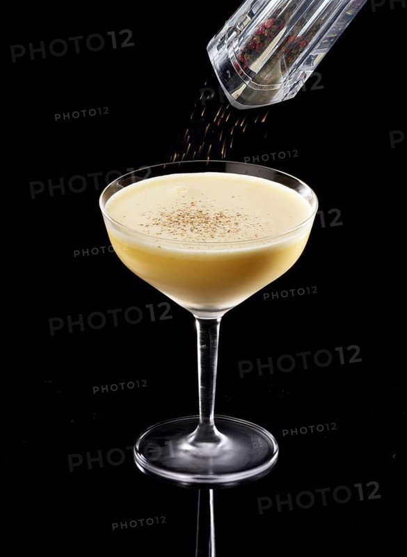 Light brown cocktail on a black background, coarsely ground pepper as garnish, studio recording