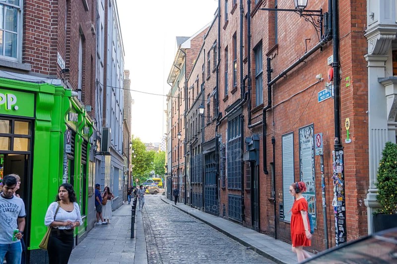 Narrow street with characteristic brick facades and passing pedestrians in the evening mood, Dublin, Ireland