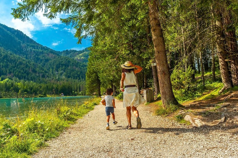 Mother and son running on a path along the shore of lake dobbiaco enjoying the tranquility of the dolomites on a beautiful summer day