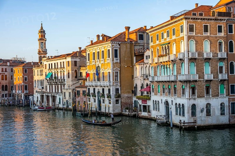 View of the Grand Canal with gondoliers at sunset, picturesque evening mood with palazzos on the canal and church tower of the Chiesa Parrocchiale dei Santi Apostoli, view from the Rialto Bridge, Venice, Veneto, Italy