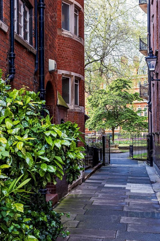 A paved lane flanked by red brick buildings leads to the entrance of Mount Street Gardens in Mayfair, London, England, United Kingdom