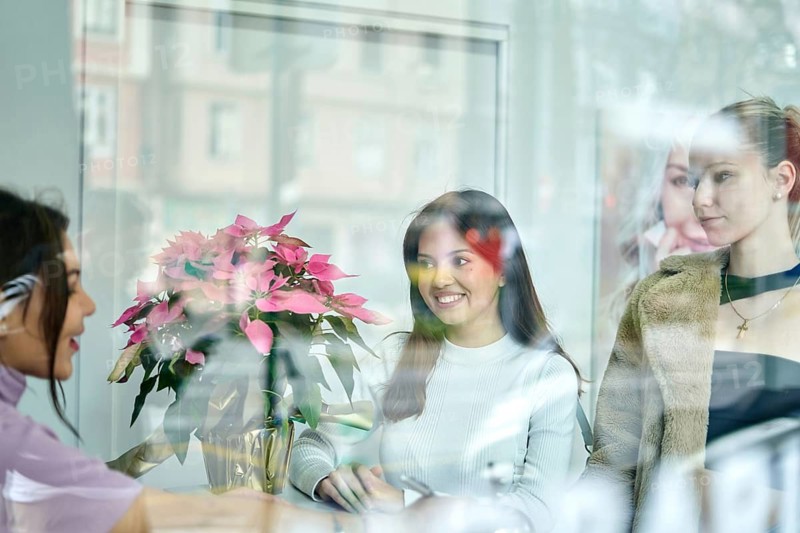 Two clients interact with a beauty consultant in a professional salon filled with natural light. Floral arrangements enhance the inviting atmosphere, creating a relaxing environment