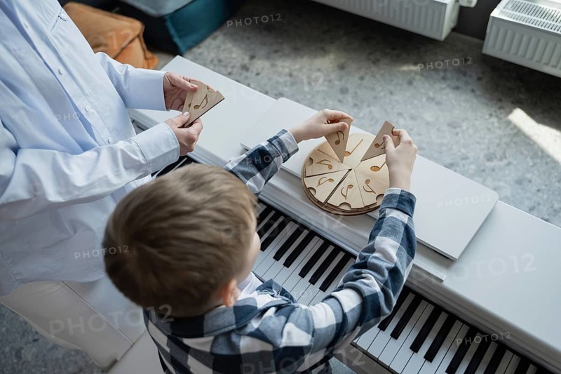 A young boy engages with music through playful learning, arranging puzzle pieces on a piano. This interactive method introduces rhythm and notes, combining fun with education