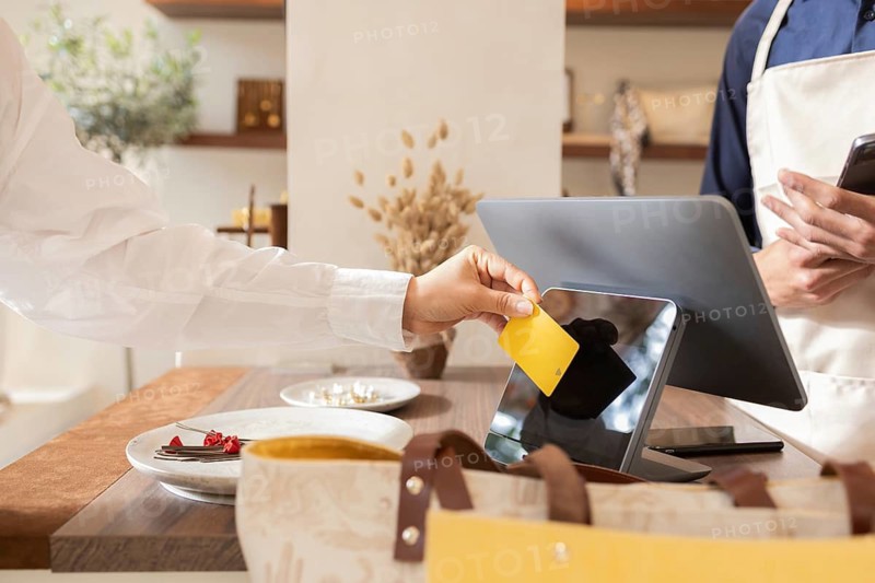 A customer makes a payment with a yellow card at an elegant bag store counter. The scene captures the modern shopping experience, combining convenience and style