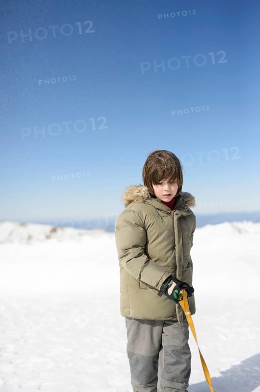 A young child in a winter coat stands amidst the snow at Sierra Nevada Ski Resort, Granada. The clear blue sky and snowy landscape highlight a delightful winter scene