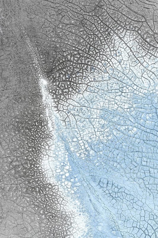 Close-up of an abstract icy surface featuring intricate crack patterns in shades of gray and blue, showcasing natural textures and fractal-like designs. Ideal for artistic backgrounds